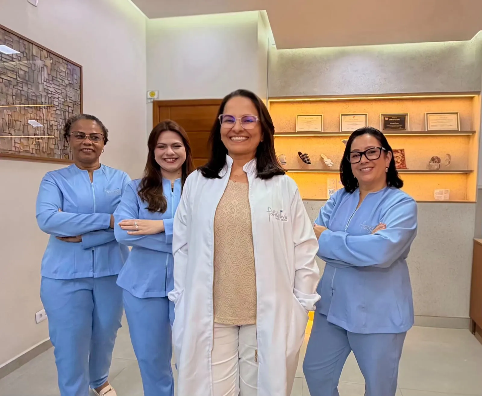 A equipe do Espaço Forma Viva reunida na recepção da clínica, com Marisabel Henrique de jaleco branco ao centro e as demais profissionais de uniforme azul